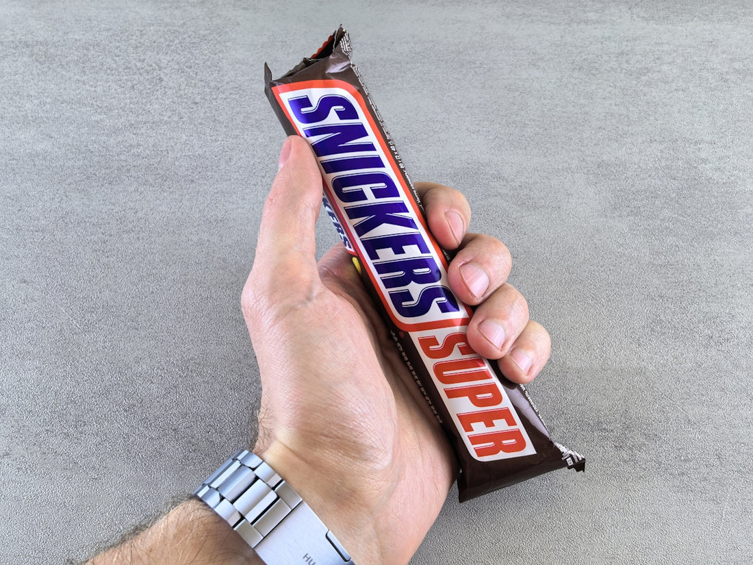 A hand holds a snickers super candy bar.